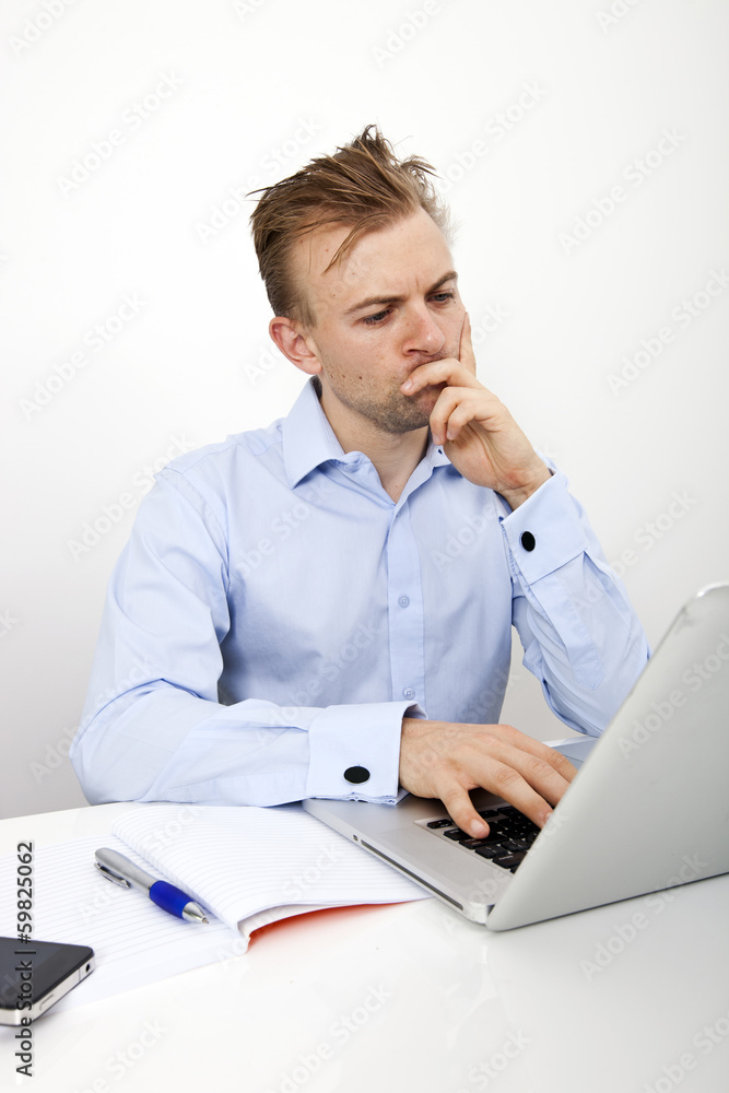Thoughtful businessman using laptop at desk in office Thoughtful businessman using laptop at desk in office