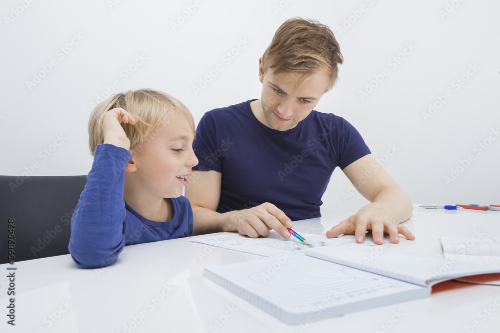 Mid adult man assisting boy in studies at table Mid adult man assisting boy in studies at table