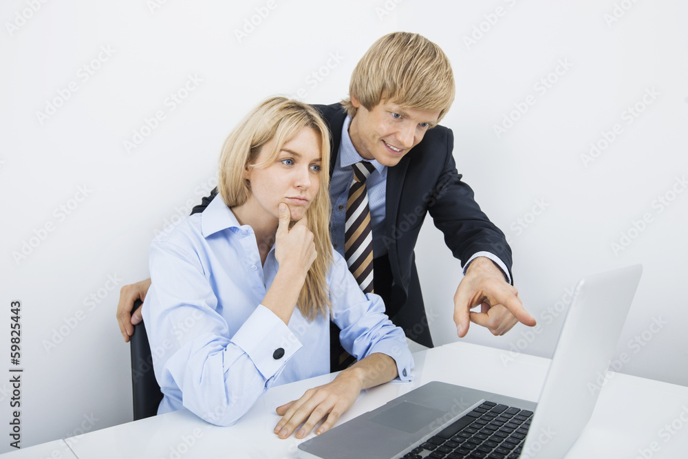 Businessman showing something to coworker on laptop in office Businessman showing something to coworker on laptop in office