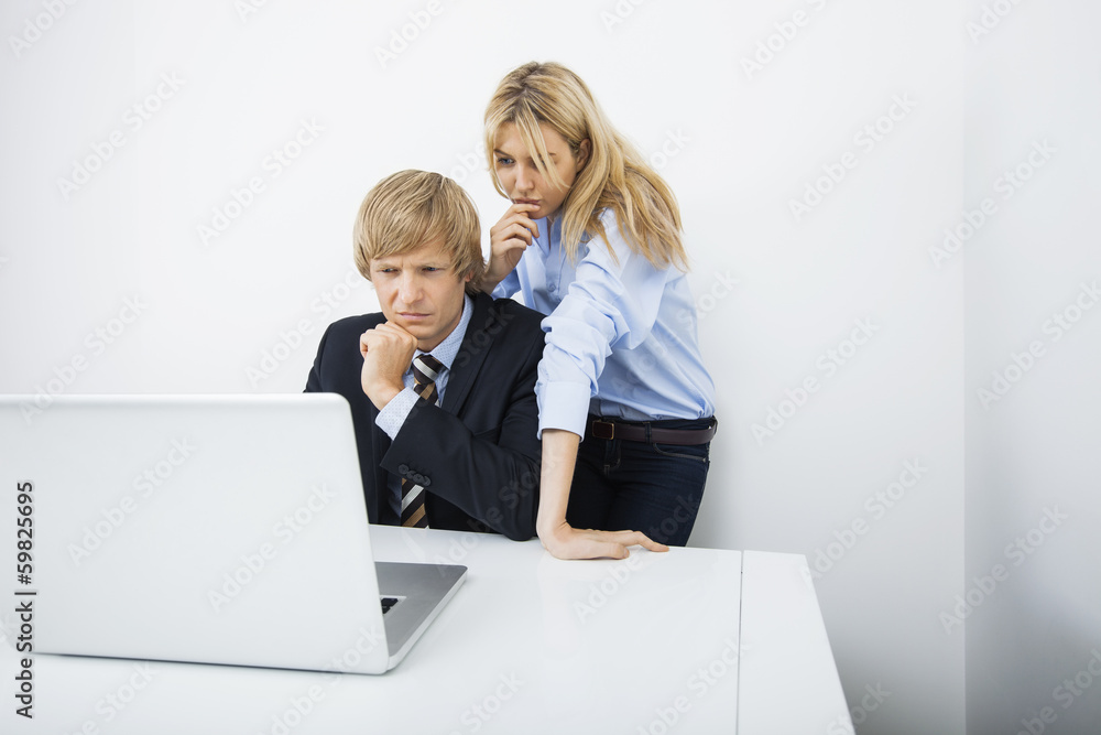 Businesspeople using laptop together at desk in office Businesspeople using laptop together at desk in office