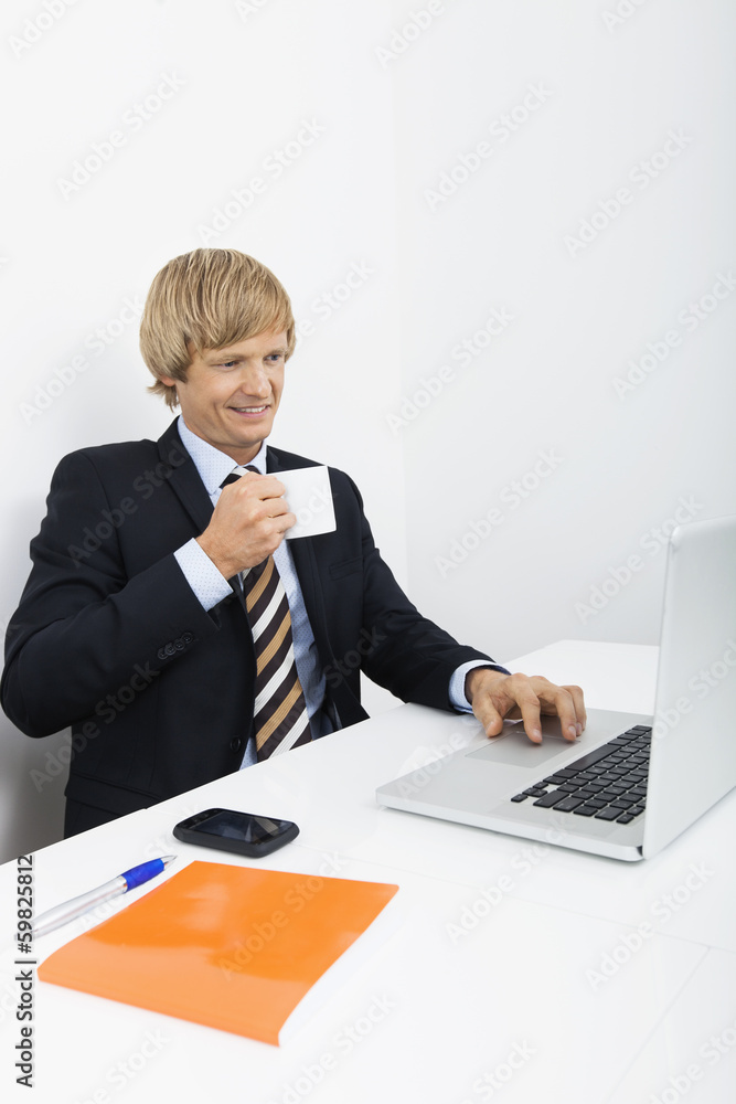 Confident businessman having coffee white using laptop in office Confident businessman having coffee white using laptop in office