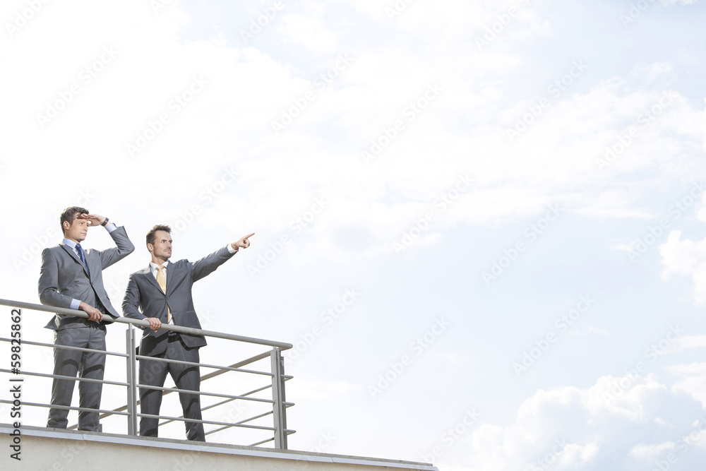 Businessman showing something to coworker against cloudy sky