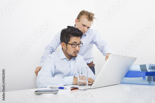 Businessmen using laptop together at desk in office