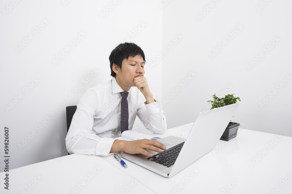 Bored mid adult businessman using laptop at desk in office Bored mid adult businessman using laptop at desk in office