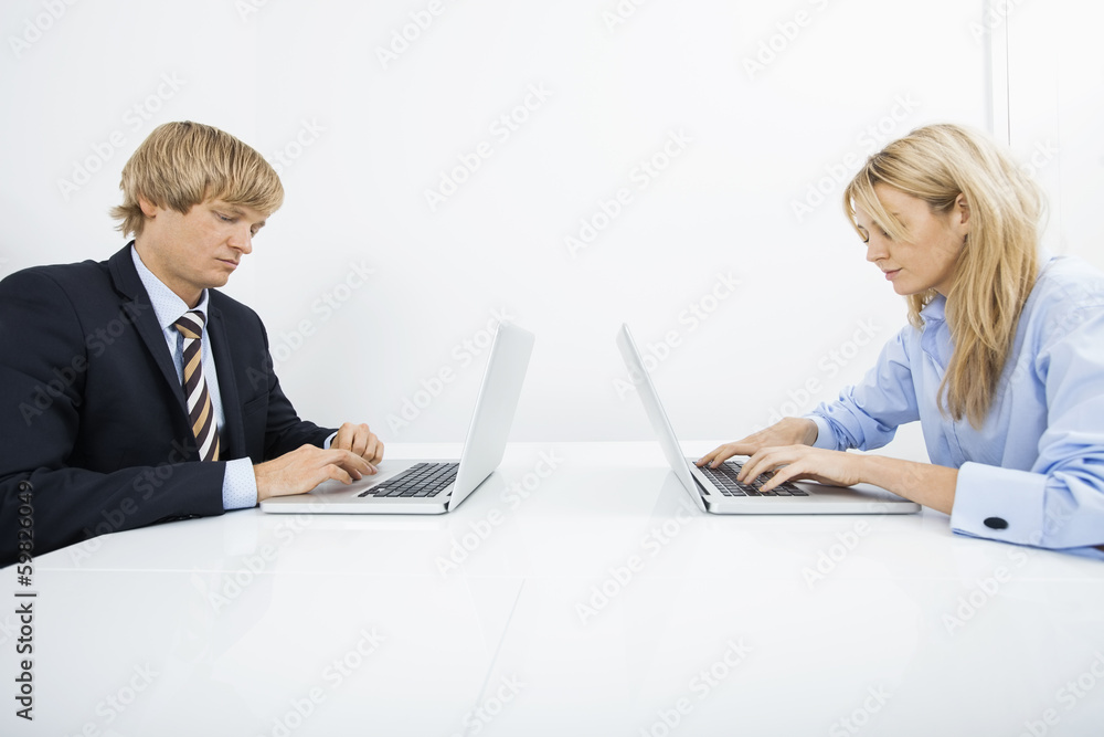 Businesspeople using laptops at desk in office Businesspeople using laptops at desk in office