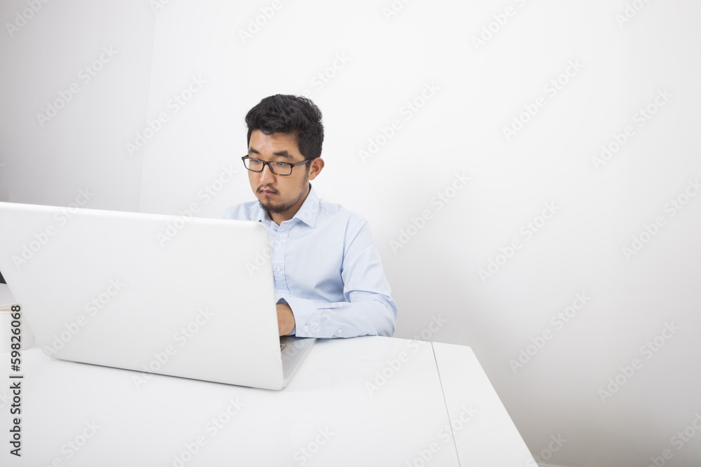 Businessman working on laptop at desk in office Businessman working on laptop at desk in office