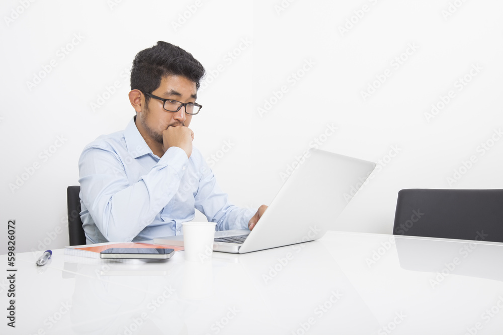 Young businessman working on laptop at desk in office Young businessman working on laptop at desk in office