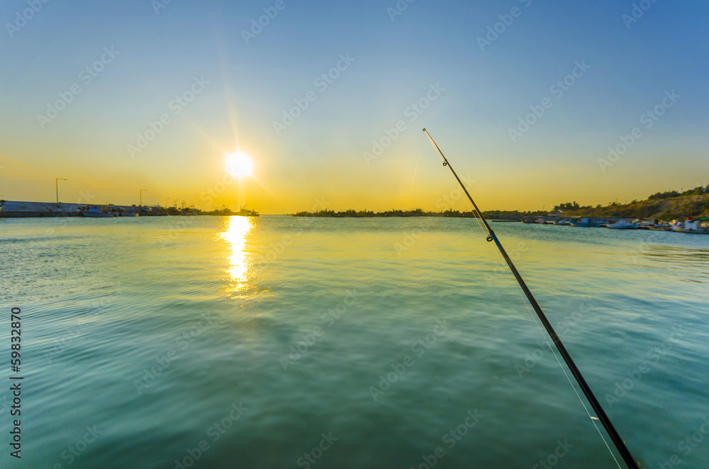 Fishing rod in ocean at dawn with colorful sky and water reflection Fishing rod in ocean at dawn with colorful sky and water reflection