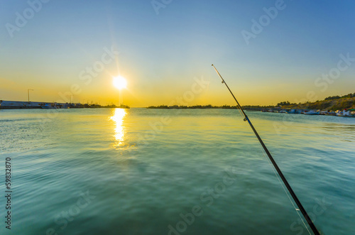 Fishing rod in ocean at dawn with colorful sky and water reflection