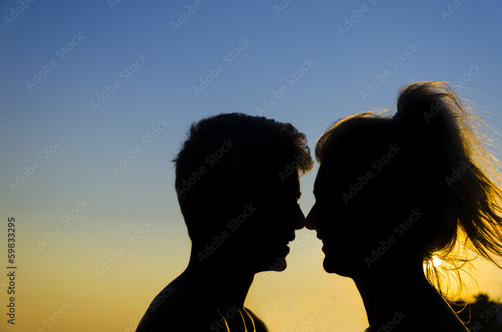 romantic couple silhouette profiles at sunset, touching noses.