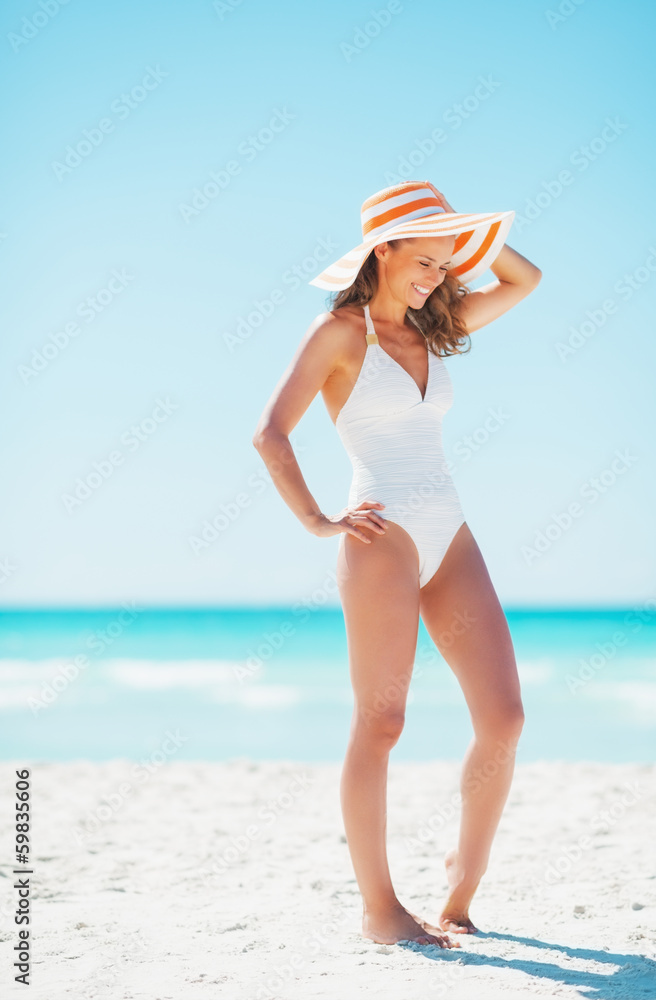 Full length portrait of smiling young woman in hat on beach
