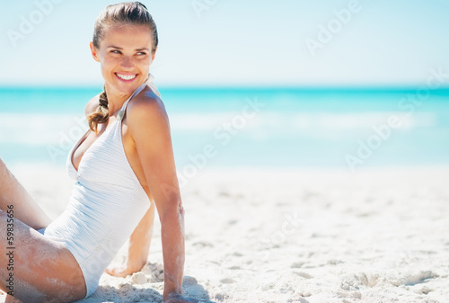 Smiling young woman sitting on beach and looking on copy space