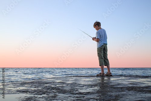 A young boy with a fishing rod fishing in the sea