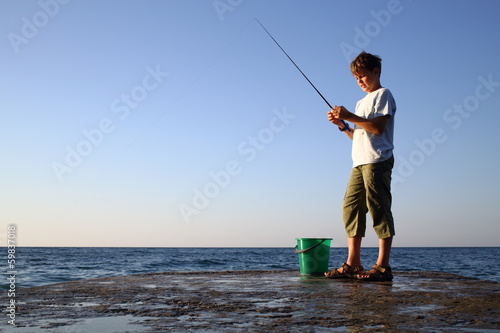 boy with a fishing rod and bucket fishing in sea with horizon