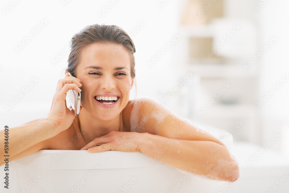 Smiling young woman talking mobile phone in bathtub Smiling young woman talking mobile phone in bathtub