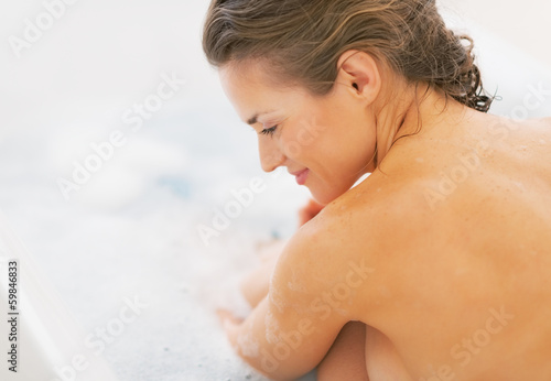 Relaxed young woman sitting in bathtub. rear view