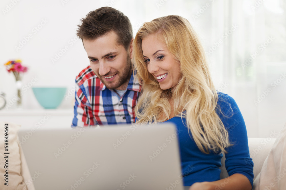 Smiling couple using laptop at home . Smiling couple using laptop at home .