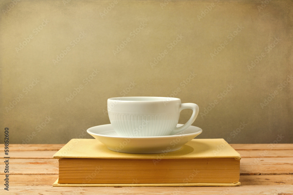 Coffee cup on book on wooden table over grunge background