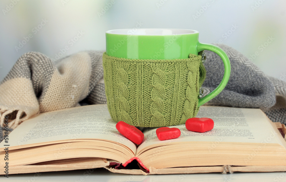 Cup with knitted thing on it and open book close up Cup with knitted thing on it and open book close up