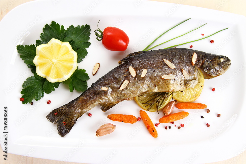 Fried trout with vegetables and split almonds on white plate Fried trout with vegetables and split almonds on white plate