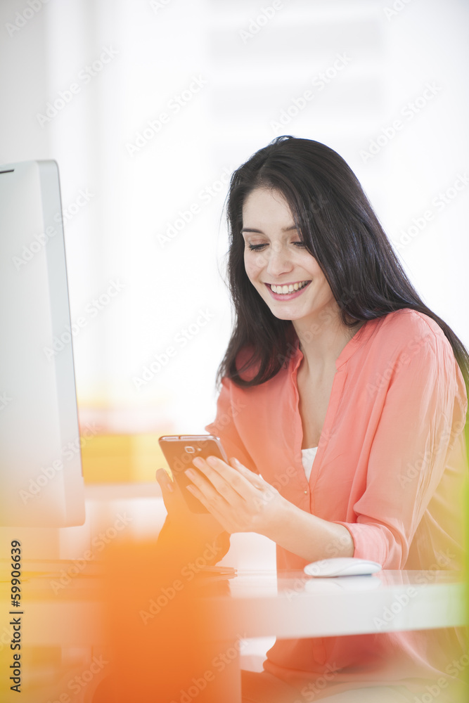 handsome woman at work in front of a computer and holding a phon handsome woman at work in front of a computer and holding a phon