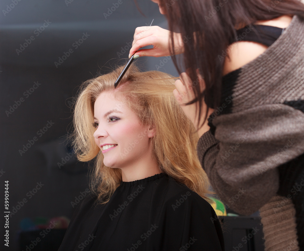Fototapeta premium Hairstylist combing client blond girl in hairdressing salon