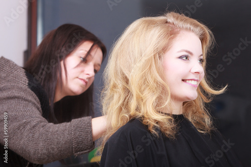 Hairstylist combing client blond girl in hairdressing salon