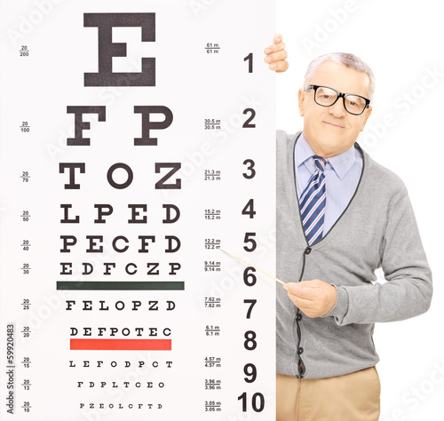 Senior man standing behind eyesight test pointing with a stick