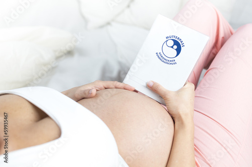 Schwangere Frau liegend hält  Babybauch und Mutterpass