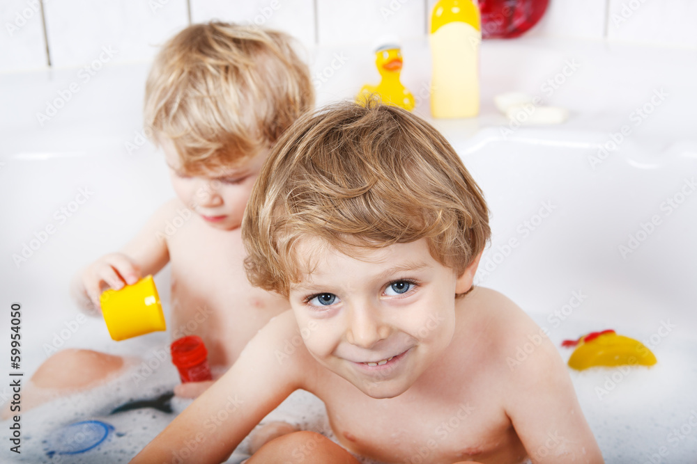 Two little twins boys having fun with water by taking bath in ba Two little twins boys having fun with water by taking bath in ba