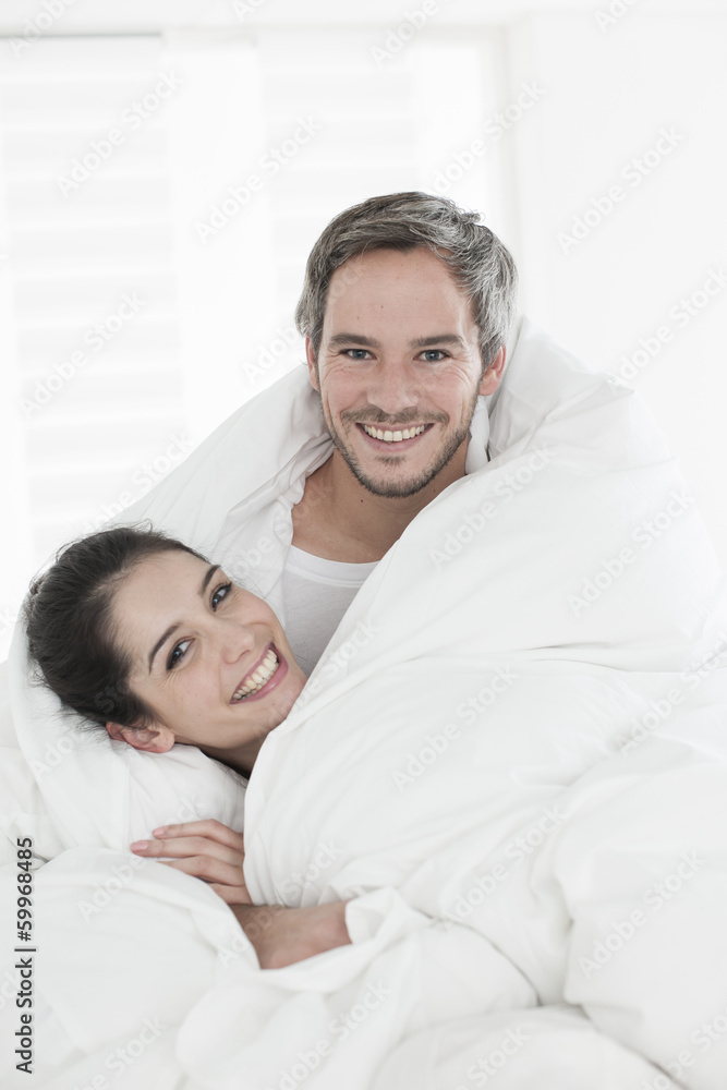 cheerful young couple wrapped in their quilt cheerful young couple wrapped in their quilt