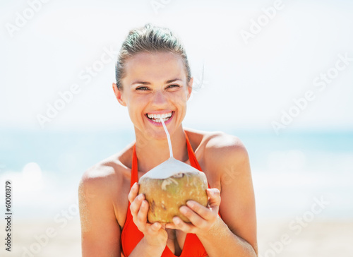 Happy young woman drinking coconut milk on beach