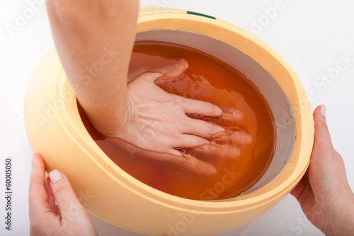 Φωτογραφία Female hand and orange paraffin wax bowl. Woman in beauty salon