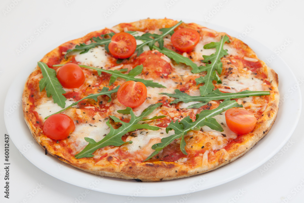Pizza with tomato and arugula on white plate