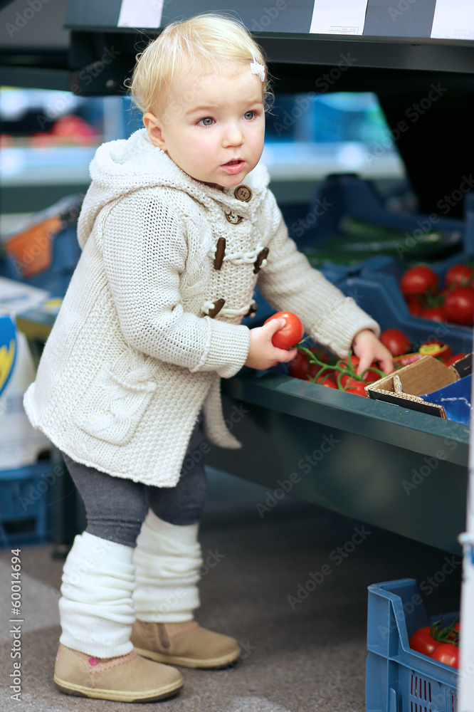 Adorable blonde toddler girl picking up tomato from a shelf Adorable blonde toddler girl picking up tomato from a shelf
