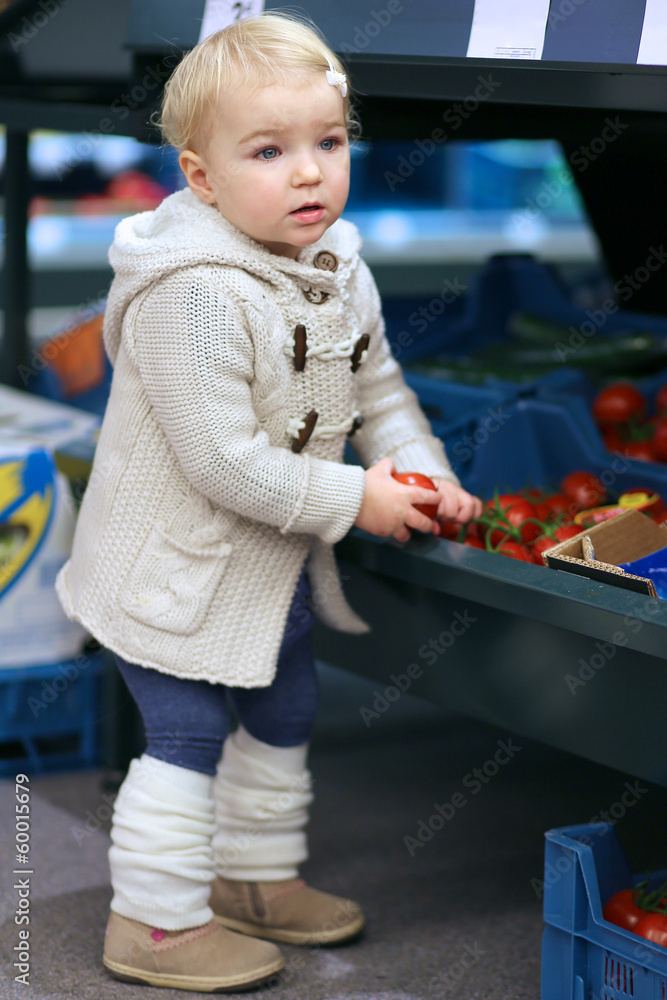 Adorable blonde toddler girl picking up tomato from a shelf Adorable blonde toddler girl picking up tomato from a shelf