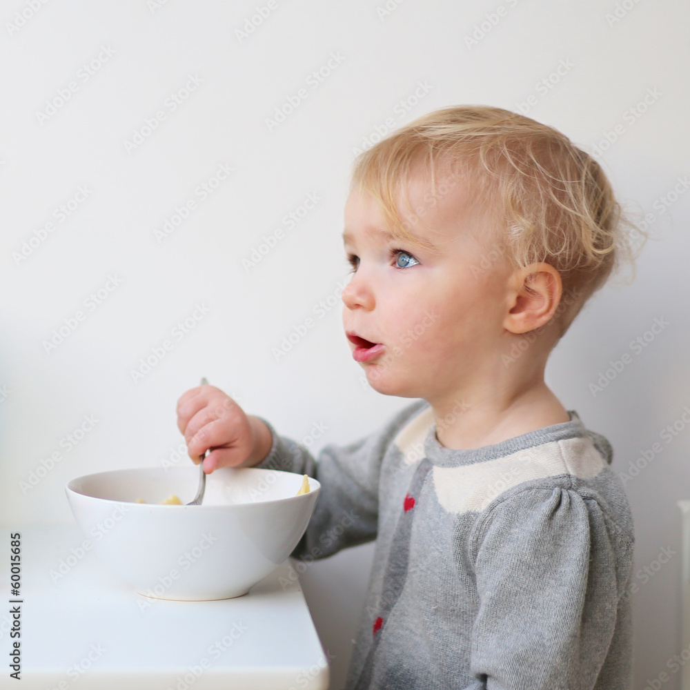 Sweet blonde toddler girl eating porridge with spoon Sweet blonde toddler girl eating porridge with spoon