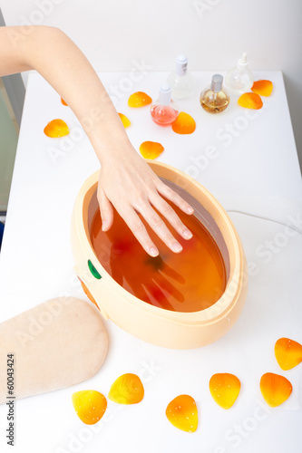 Tela Female hand and orange paraffin wax bowl. Woman in beauty salon