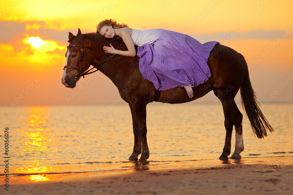 Beautiful woman riding a horse at sunset on the beach. Young bea Beautiful woman riding a horse at sunset on the beach. Young bea