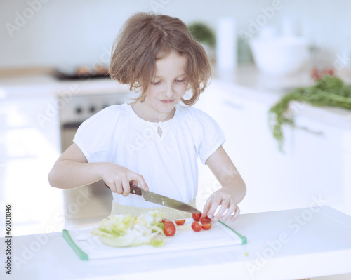 Young girl chopping tomatoes and making a salad in the kitchen