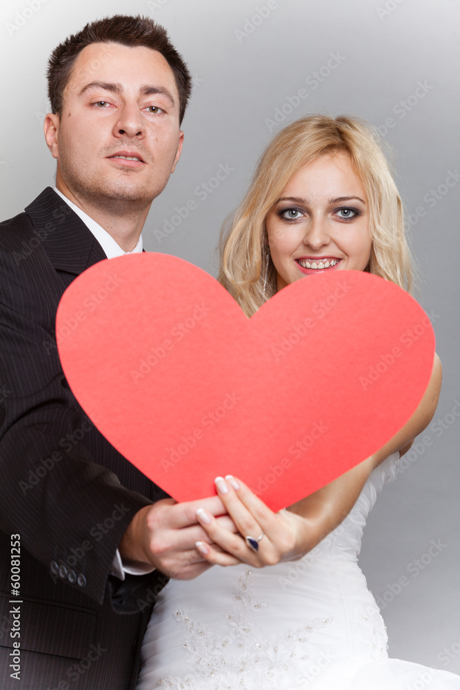 Portrait of happy bride and groom with red heart on gray Portrait of happy bride and groom with red heart on gray