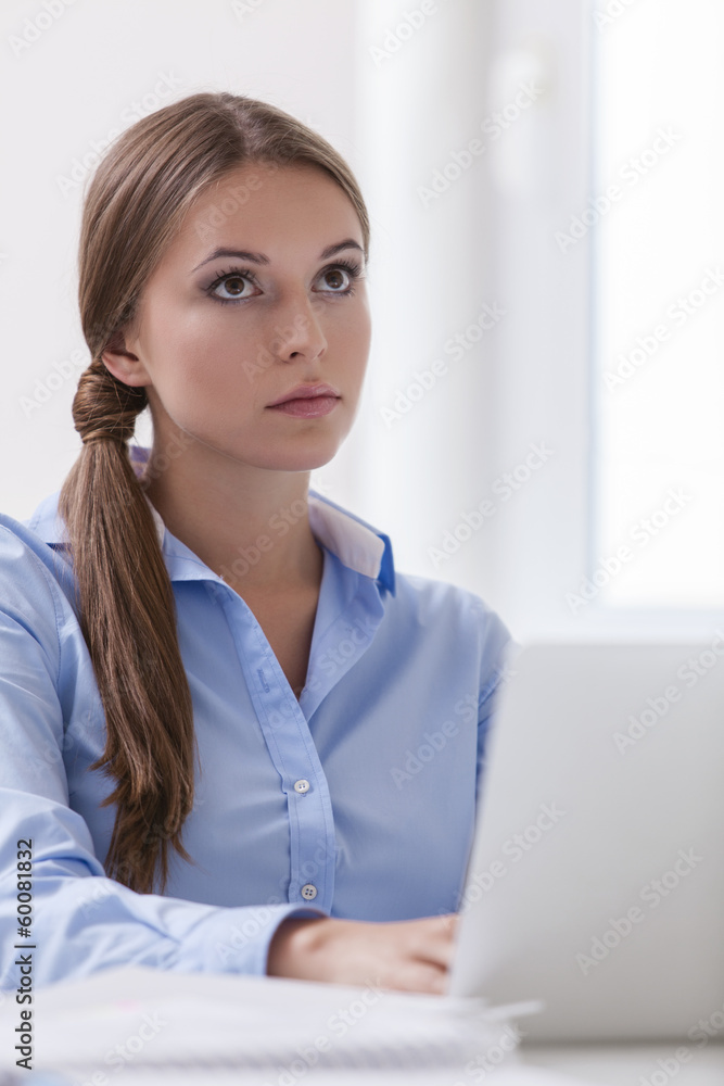Beautiful businesswoman sitting on desk and looking at laptop Beautiful businesswoman sitting on desk and looking at laptop