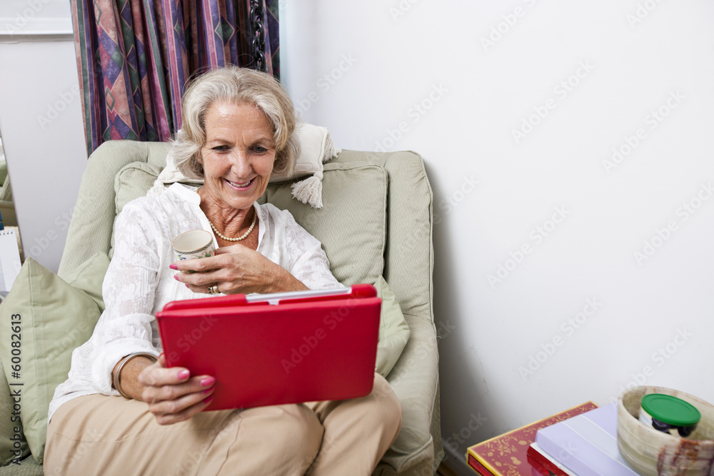 Happy senior woman looking at digital tablet on armchair in house Happy senior woman looking at digital tablet on armchair in house