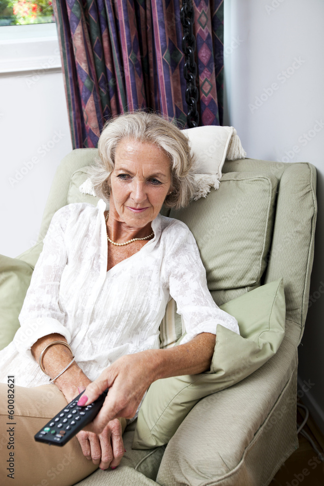 Senior woman changing channels with remote control on armchair at home Senior woman changing channels with remote control on armchair at home
