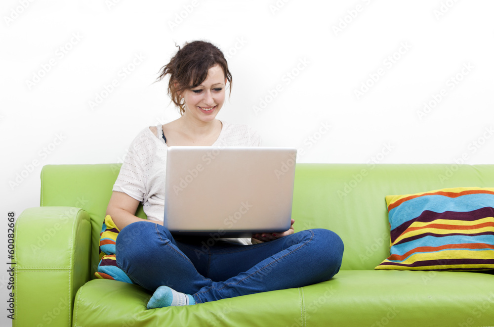 Full length of happy young woman using laptop while sitting on green sofa Full length of happy young woman using laptop while sitting on green sofa