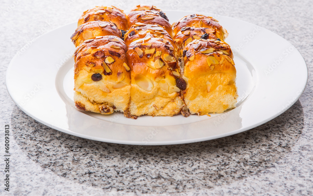 Homemade sweet bun with almond and raisins on a white plate Homemade sweet bun with almond and raisins on a white plate
