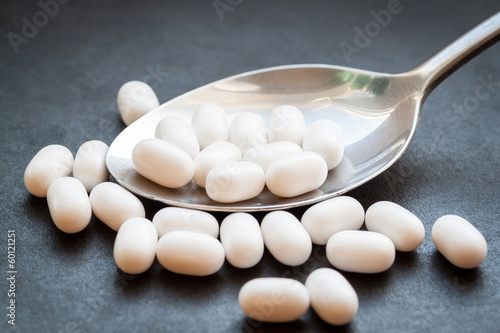 White pills in spoon on dark background.