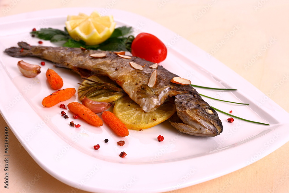 Fried trout with lemon and split almonds on white plate