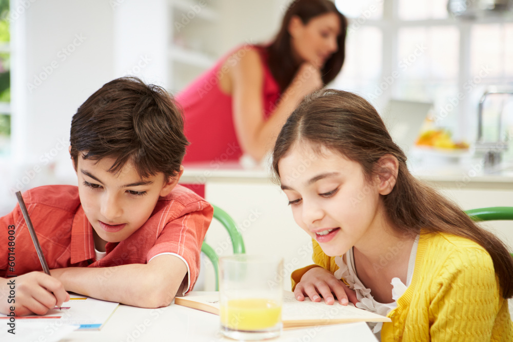 Children Doing Homework As Mother uses Laptop In Background Children Doing Homework As Mother uses Laptop In Background