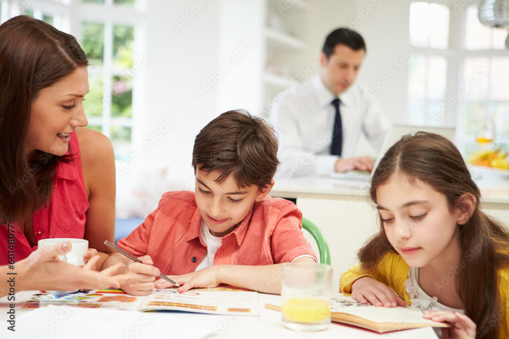 Mum Helps Children With Homework As Dad Works In Background